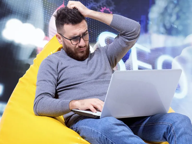Gondolkodó férfi laptop használata közben, a kép azt szemlélteti, miért nem működik a keresőoptimalizálás, amikor a túl sok ellentmondó tanács megnehezíti a helyes irány kiválasztását