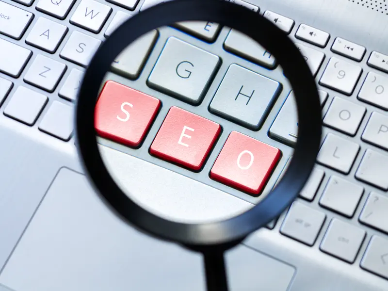 SEO kulcsszó kannibalizáció vizuális ábrázolása, nagyítóval kiemelt SEO billentyűk, a relevancia megoszlását szimbolizálva